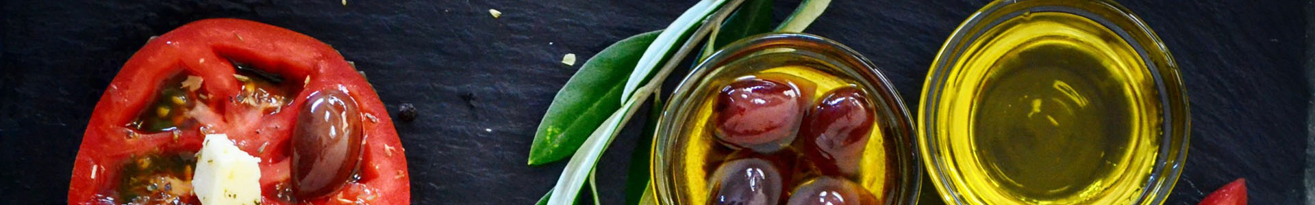 Olivenöl im Glas mit Olvien und Tomaten serviert